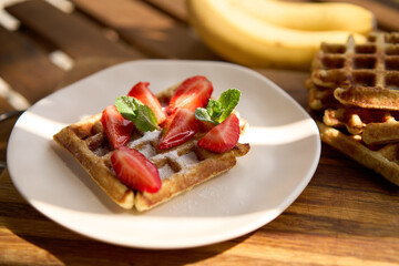 Closeup view of breakfast belgium waffles with strawberry and banana with mint on wooden background. High quality photo