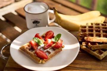Closeup view of breakfast belgium waffles with strawberry and banana with mint on wooden background. High quality photo