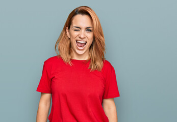Hispanic young woman wearing casual red t shirt winking looking at the camera with sexy expression,...