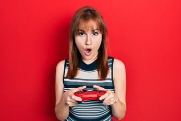 Redhead young woman playing video game holding controller afraid and shocked with surprise and amazed expression, fear and excited face. © Krakenimages.com
