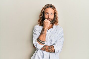 Handsome man with beard and long hair wearing casual white shirt thinking concentrated about doubt with finger on chin and looking up wondering