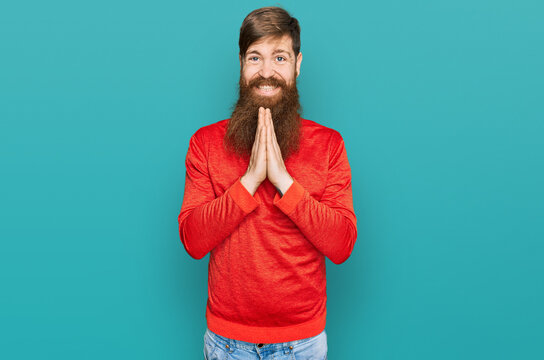 Redhead man with long beard wearing casual clothes praying with hands together asking for forgiveness smiling confident.