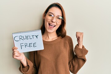 Young caucasian woman holding cruelty free message paper pointing thumb up to the side smiling...