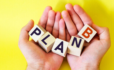 Business strategy and marketing concept, wooden cubes with plan b in the hands of a man on a yellow background