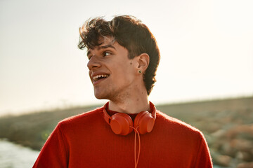 Young hispanic man smiling happy using headphones at the beach