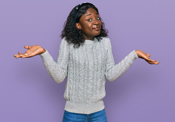 Beautiful african young woman wearing casual winter sweater clueless and confused expression with...