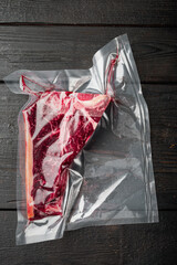 Raw beef steak t-bone or porterhouse in vacuum Pack, on black wooden background, top view flat lay