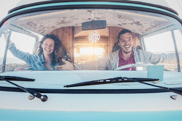 Happy travel couple having fun driving vintage minivan during road trip tour - Youth people vacations lifestyle concept