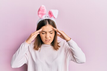 Young beautiful woman wearing cute easter bunny ears with hand on head for pain in head because...
