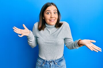 Young beautiful woman wearing casual turtleneck sweater clueless and confused expression with arms and hands raised. doubt concept.