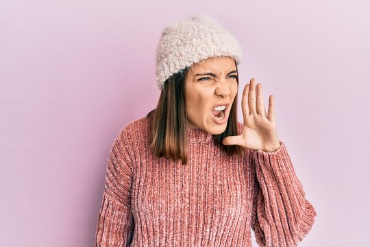 Young beautiful woman wearing wool sweater and winter hat shouting and screaming loud to side with hand on mouth. communication concept.