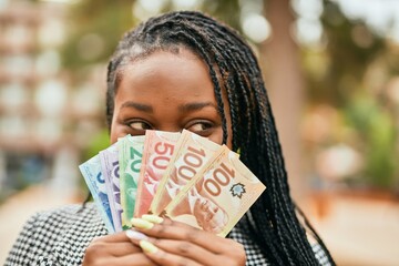 Young african american businesswoman smiling happy covering face with canadian dollars at the park.