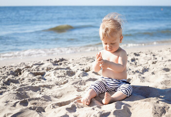 10 month old blond boy playing with sand on the beach