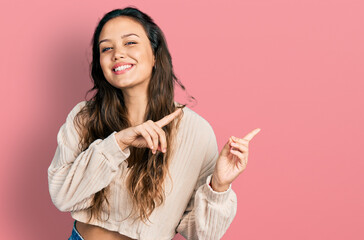 Young hispanic girl wearing casual clothes smiling and looking at the camera pointing with two hands and fingers to the side.