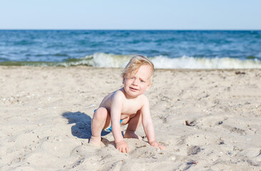 happy, smiling boy on the beach. 10 month old blond boy crawling on the beach