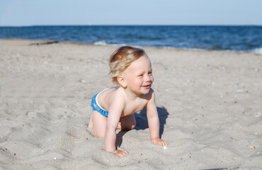 happy, smiling boy on the beach. 10 month old blond boy crawling on the beach
