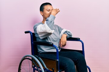Beautiful hispanic woman with short hair sitting on wheelchair smelling something stinky and...