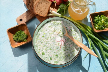 Cold soup okroshka with sausage, potato, egg, radish, cucumber, greens and kvass in a bowl, bread...