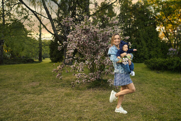 Mother and baby in blooming garden. Mom and child in spring. Springtime family scene. Flowers of apple or cherry tree. High quality photo