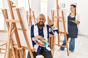 Obraz premium Senior artist man at art studio gesturing finger crossed smiling with hope and eyes closed. luck and superstitious concept.