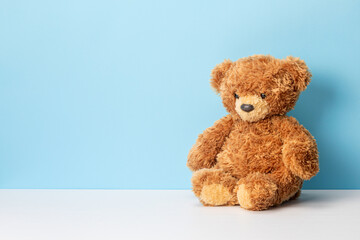 Teddy bear sits on a white table and blue background. Template Copy space for text