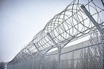 Prison fence. Grid fence with barbed wire against sunset. Barbed wire. Security measures for...