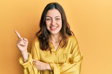 Young brunette woman wearing casual yellow shirt smiling happy pointing with hand and finger to the side