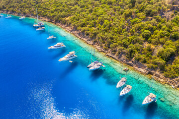 Fototapeta na wymiar Aerial view of beautiful yachts and boats on the sea bay at sunset in summer. Gemiler Island in Turkey. Top view of luxury yachts, sailboats, clear blue water, beach, mountain and green forest. Nature
