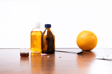 Various medicines on the table. Syrups and a pill on the table. Medicines and an orange.