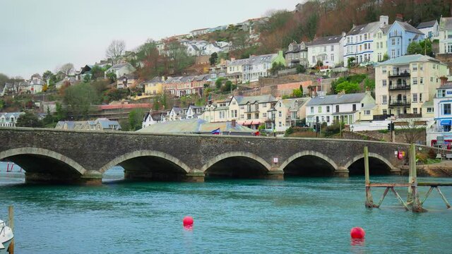 Old British bridge in Looe Harbour with blue waters of East River with boats, vessels in the center of coastal Town - South East Cornwall, England in 4K. English houses by the River.