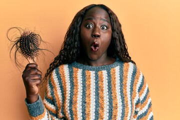 African young woman holding comb loosing hair scared and amazed with open mouth for surprise,...