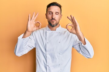 Handsome man with beard wearing professional cook uniform relax and smiling with eyes closed doing meditation gesture with fingers. yoga concept.