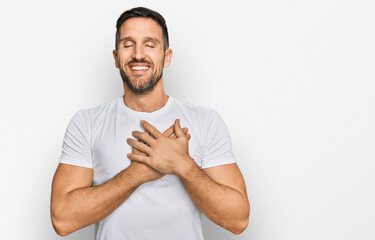 Handsome man with beard wearing casual white t shirt smiling with hands on chest with closed eyes and grateful gesture on face. health concept.