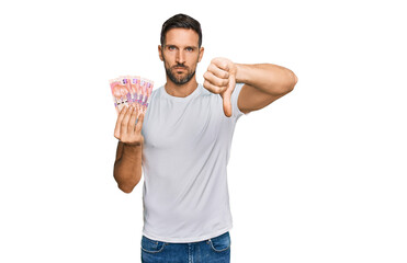 Handsome man with beard holding south african 50 rand banknotes with angry face, negative sign showing dislike with thumbs down, rejection concept