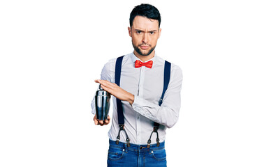 Hispanic man with beard preparing cocktail mixing drink with shaker skeptic and nervous, frowning...