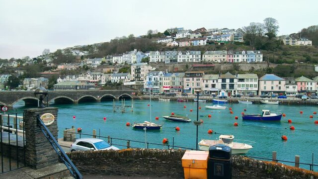 Looe Harbour and blue waters of East River with boats, vessels in the center of Looe coastal Town - South East Cornwall, England in 4K. A blue river with old English houses on the seashore edge.