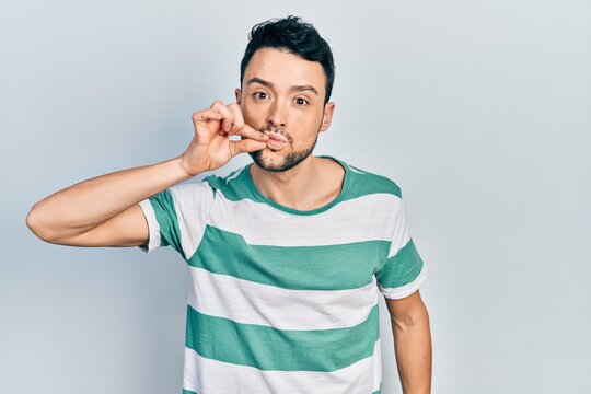 Young hispanic man wearing casual clothes mouth and lips shut as zip with fingers. secret and silent, taboo talking