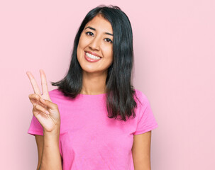 Beautiful asian young woman wearing casual pink t shirt showing and pointing up with fingers number two while smiling confident and happy.