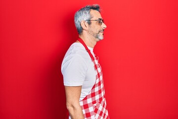 Handsome middle age man with grey hair wearing apron looking to side, relax profile pose with natural face with confident smile.