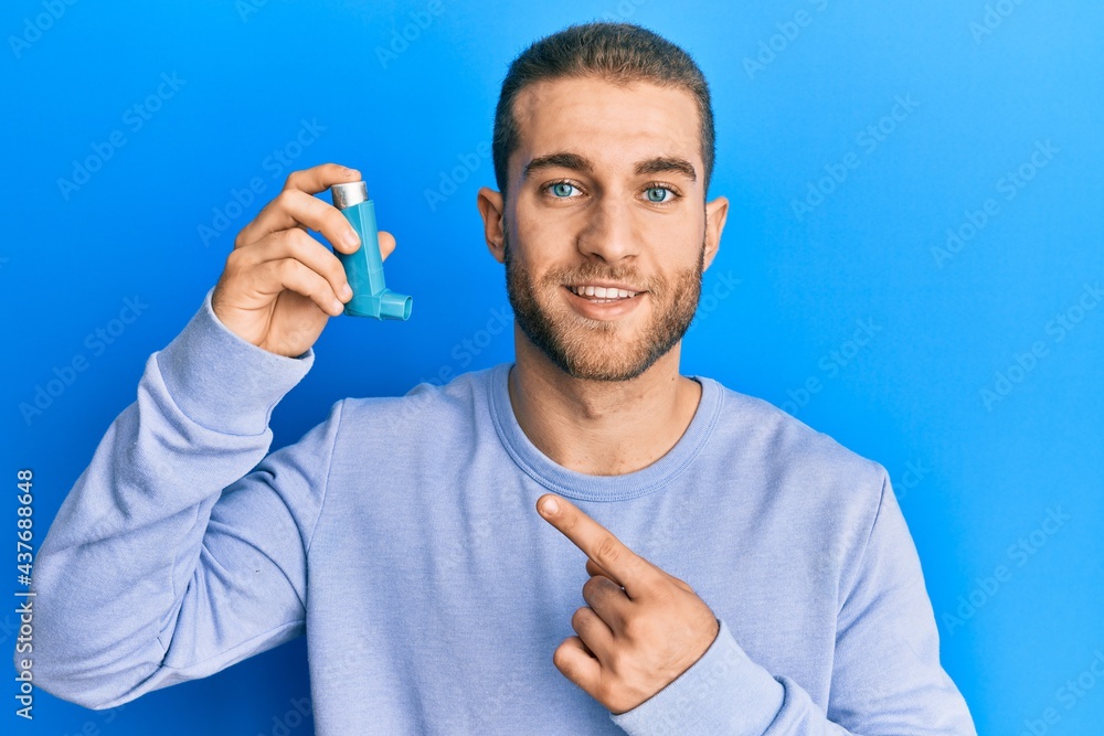 Canvas Prints Young caucasian man holding medical asthma inhaler smiling happy pointing with hand and finger