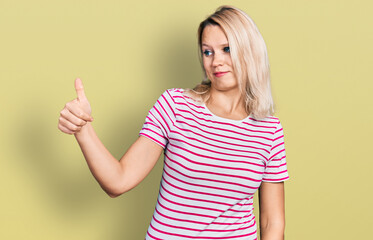 Young caucasian woman wearing casual clothes looking proud, smiling doing thumbs up gesture to the side