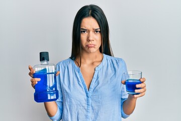 Young hispanic girl holding mouthwash for fresh breath depressed and worry for distress, crying...