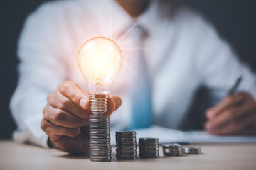 Businessman hand holding light bulb with line connect and Coins stack on the wooden table, Saving...