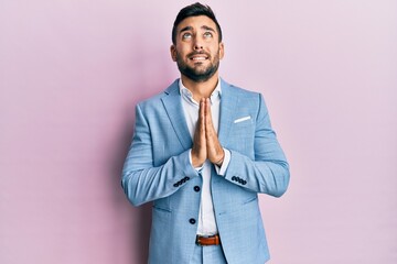 Young hispanic businessman wearing business jacket begging and praying with hands together with hope expression on face very emotional and worried. begging.