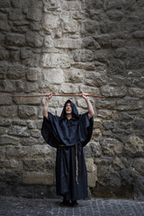 The monk holds his staff high against the textured stone wall, the light descending on him from above. Concept: prayer and magic, descent of the spirit, God's protection and healing.