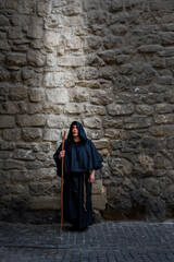 A monk with a staff at a textured stone wall, light falling on him from above. Concept: prayer and magic, the descent of the spirit, God's protection and healing, the power of prayer.