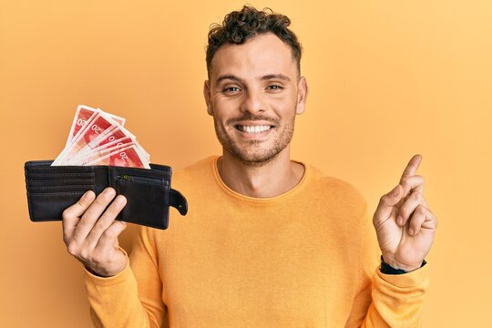 Young hispanic man holding wallet with israel shekels smiling happy pointing with hand and finger to the side