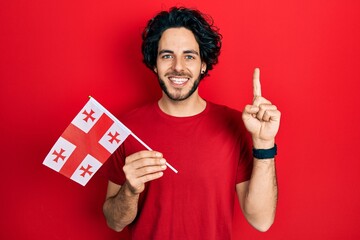 Handsome hispanic man holding georgia flag smiling with an idea or question pointing finger with happy face, number one