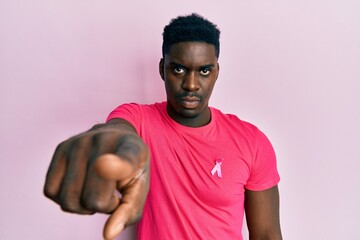 Handsome black man wearing pink cancer ribbon attached on shirt pointing with finger to the camera...