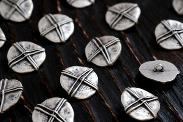 Sewing buttons made of white metal on a wooden surface of dark brown color. Sewing accessories. Design elements and decoration of clothing for women.